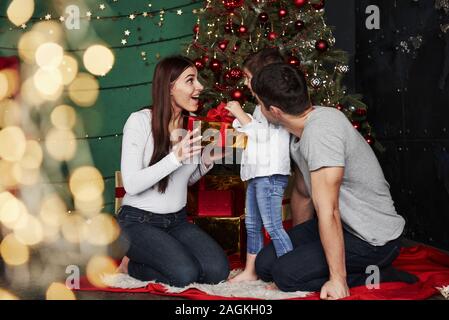 Überrascht. Sehr nette Familie sitzt in der Nähe der Weihnachtsbaum mit Geschenkboxen im Winter am Abend, genießen die Zeit zusammen verbringen Stockfoto