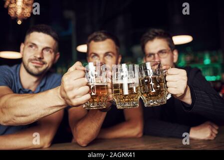 Klopfen Gläser. Drei sport Fans in einer Bar beobachten Fußball. Mit einem Bier in der Hand Stockfoto