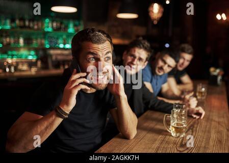 Man spricht von dem Telefon. Drei sport Fans in einer Bar beobachten Fußball. Mit einem Bier in der Hand Stockfoto