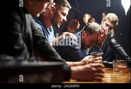 Mann fühlt sich schrecklich. Freunde in der Kneipe mit Alkohol ruht in den Händen. In Gespräch Stockfoto