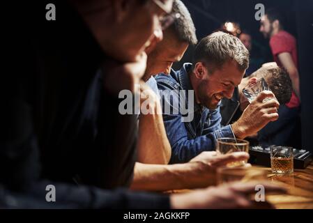 Von der Seite. Freunde in der Kneipe mit Alkohol ruht in den Händen. In Gespräch Stockfoto