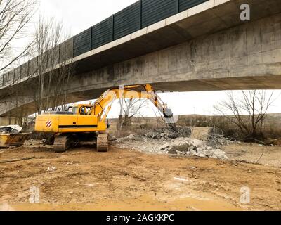 Ein Bagger mit einem konkreten Abriss mit einem Hydraulikhammer unter einer Brücke im Bau. Baustelle Stockfoto