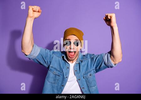 Foto der Trendfarbe Weiß fröhliche stattlicher Mann mit Händen zu schreien, schreien mit Fäusten, lächelnd toothily feiern Sieg über Violett isoliert Stockfoto