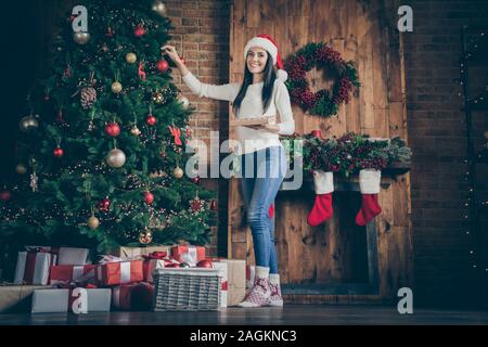 Voller Körper Foto von positiven Fröhliche braune Haare Mädchen bereiten sich für x-mas Zeit party Feier Weihnachten Baum mit Bällen Spielzeug im Haus dekorieren mit Stockfoto