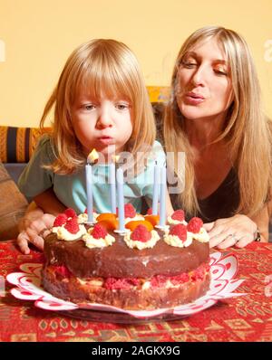 Junge mit langen blonden Haaren ausblasen Kerzen auf dem Geburtstagskuchen Stockfoto