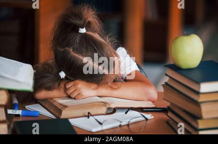 Schlafen auf dem Tisch. Süße kleine Mädchen mit Zöpfen ist in der Bibliothek. Apple auf der Bücher Stockfoto