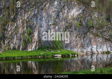 Sommer Blick auf die Felsen in der Nähe des Flusses. Ein Felsen mit einem noch abfallende Flanke in der Nähe von einem ruhigen Fluss. Stockfoto