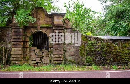 Ein teilweise bis Gateway in einem Bemoosten Wand blockiert bewacht den verwilderten Garten der aufgegebenen Courthill House Mansion neben der A896 Straße an Kis Stockfoto