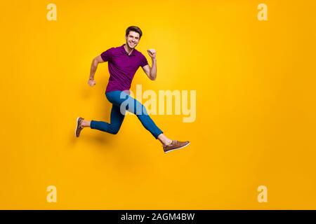 Volle Länge Körpergröße phoo fröhliche Braunhaarige attraktiver Mann mit blauen Hosen Hose lila t-shirt Schuhe strebende springen laufen Stockfoto
