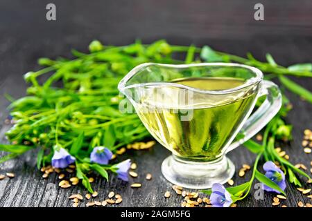 Leinöl in einem Glas Sauciere mit Samen, Blätter und Flachs Blumen auf Holzbrett Hintergrund Stockfoto