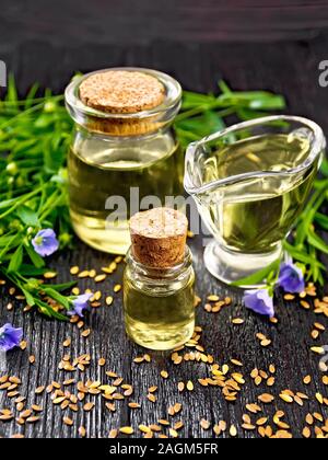 Leinöl in zwei Gläser und eine Sauciere mit Samen, Blättern und blauen Flachs Blumen auf dunklen Holzplatte Hintergrund Stockfoto