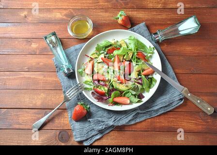 Avocado-Salat mit Erdbeeren, Blauschimmelkäse, Rucola und Rübenblättern auf Holzhintergrund. Gesunde Schüssel zum Mittagessen Stockfoto