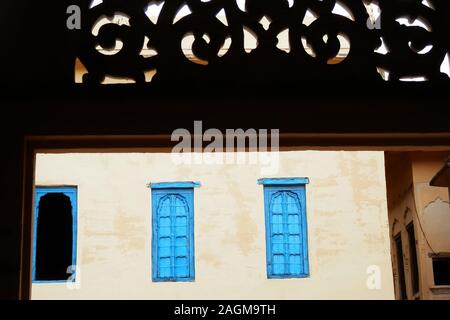 Bunte blue windows durch ein Fenster mit ornamentalen Schnitzereien gesehen, in einem Dorf in der Wüste Thar, Rajasthan, Nordindien. Stockfoto