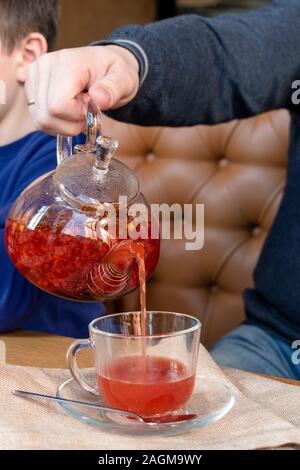 Männliche hand gießt roter Tee aus einer Teekanne in eine Schale. Stockfoto