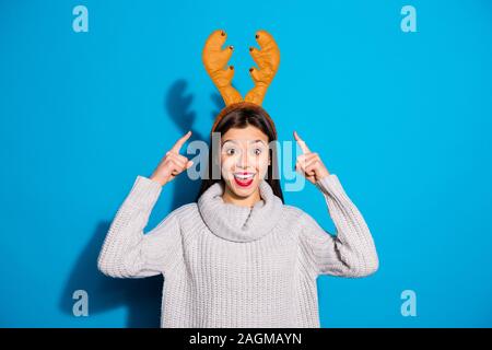 Foto der hübschen Dame zeigt auf ihrem Kopf tragen Spielzeug Hörner Strickpullover isoliert blauer Hintergrund Stockfoto