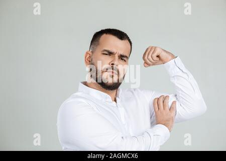 Muskulöse bärtiger Mann zeigt Bizeps auf grauem Hintergrund. Stockfoto