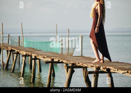 Zugeschnittenes Bild der Barefoot Frau in baumwolle kleid Wandern auf schmalen handgefertigten Holzmöbeln Pier Stockfoto