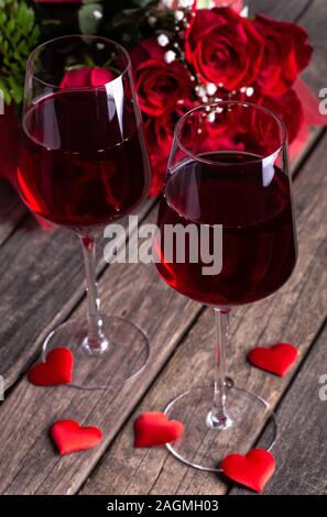 Nahaufnahme von zwei Gläser Wein mit Bouquet von roten Rosen im Hintergrund auf Holzmöbeln im Landhausstil Oberfläche Stockfoto