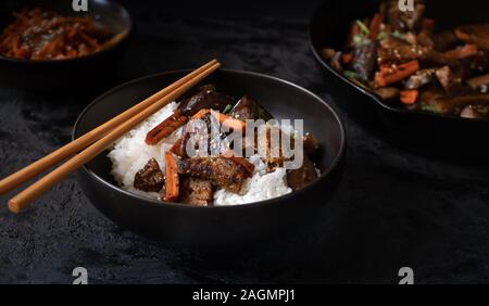 Vegan koreanischen Seitan, Karotte und Auberginen Braten über Reis mit Kimchi in einem schwarzen Schüssel Stockfoto