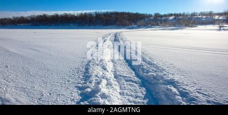 Trail von einem Schneemobil auf einem gefrorenen und Snowy River Bed. Panoramablick auf den Fluss. Norwegen Stockfoto