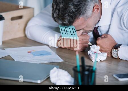 Geschäftsmann mit Zettel auf der Stirn in der Nähe von Papier Kugeln Tabelle Stockfoto