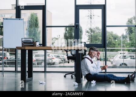 Unternehmer sitzen auf dem Boden in der Nähe der Tabelle in modernen Büro betonte Stockfoto