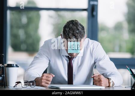 Geschäftsmann mit Zettel auf der Stirn sitzt in der Nähe von Tabelle Stockfoto