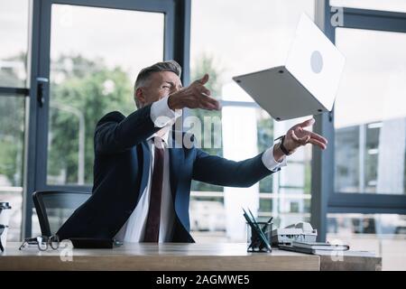 Emotionale Geschäftsmann werfen in Luft Laptop im Büro Stockfoto