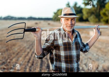 Gerne älterer Mann mit Rake in der Nähe von Feld Stockfoto