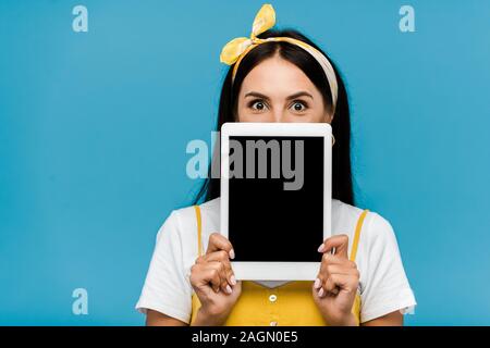 Frau mit Gesicht halten digitale Tablette mit leeren Bildschirm isoliert auf Blau Stockfoto