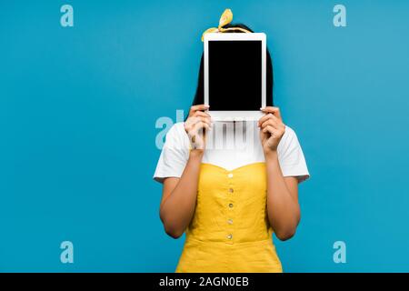 Junge Frau mit Gesicht mit digitalen Tablette mit leeren Bildschirm isoliert auf Blau Stockfoto