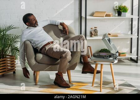 Senior afrikanische amerikanische Mann in stilvoller Kleidung im Sessel sitzen und hören Musik auf Plattenspieler Stockfoto