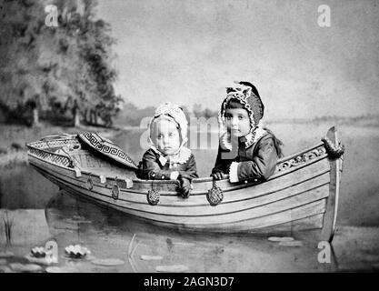 Zwei kleine Kinder posieren in einem Kunstboot für ein Farbportrait, ca. 1890. Stockfoto