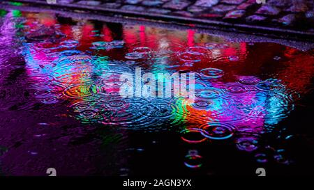 Regentropfen und Pfütze nachts mit reflektierenden farbigen Lichter von einem fairen Stockfoto