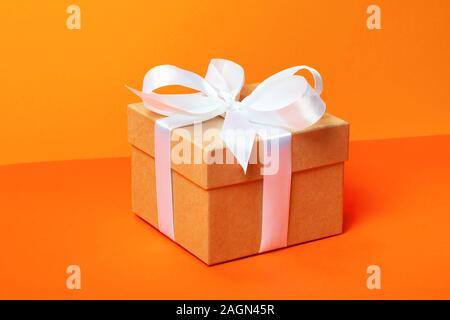 Trendige attraktive minimalistische Geschenk auf dem orangen Hintergrund. Frohe Weihnachten, Valentinstag, Geburtstag und andere Feiertage Konzept. Stockfoto