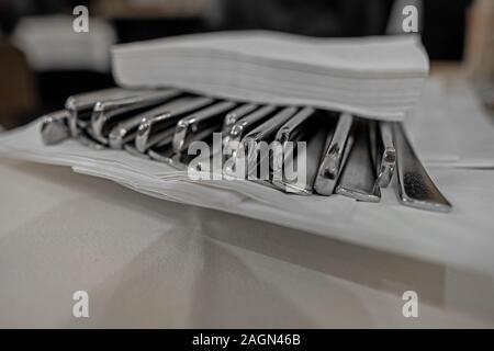 Gabeln und Messer auf einem Teller mit Weiß Servietten angeordnet auf einem reatsaurant Tisch mit Tischdecke aus Baumwolle Stockfoto