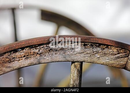 Nahaufnahme der Ein altes Wagenrad aus Holz mit Bügeleisen Gehäuse, verwitterte morsches Holz rostigem Eisen, eine zweite als Silhouette auf der Rückseite Stockfoto