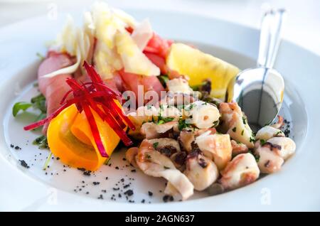 Meeresfrüchte Salat in weiße Platte closeup serviert. Octopus und Thunfisch mit Zitrone Salat Vorspeise am Tisch im Restaurant. Mediterrane Küche Rezept. Luxur Stockfoto