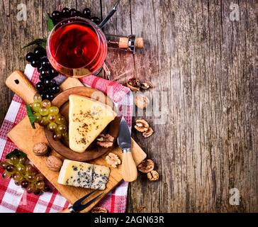 Blick von oben auf die roten Wein, Trauben und Käse auf rustikalen Holztisch Hintergrund mit Copyspace. Französische Küche Produkt von oben. Wein und Speisen immer noch Leben. Stockfoto