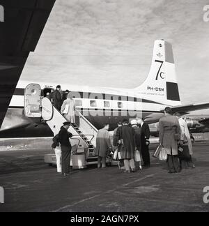 1950s, historische Passagiere, die an Bord eines Dougas DC-7C KLM-Flugzeugs am Flughafen von Anchorage, Alaska, USA, gehen. Die 1956 eingeführte DC-7C (Seven Seas) war eine Variante mit erweiterter Reichweite des ursprünglichen DC-7-Flugzeugs, mit verbesserten Motoren und zusätzlicher Kraftstoffkapazität, was ihr eine durchnon-stop transatlantische Kapazität verleiht und um europäische Fluggesellschaften anzuziehen wurde. Stockfoto