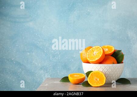 Mandarinen und Schüssel auf graue Tabelle vor blauem Hintergrund, Platz für Text Stockfoto