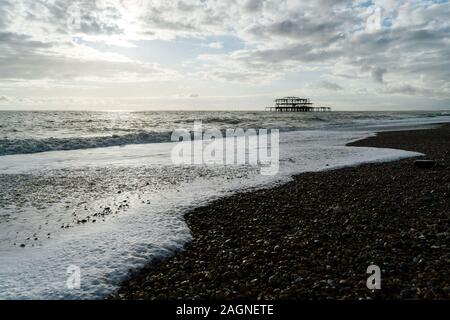 BRIGHTON, Großbritannien - 03.November 2019: Reste von Brighton Pier. Die Silhouetten, die laufen am Strand, Wellen erzeugen Wellen am Ufer, Ocean Spa Stockfoto