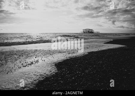 BRIGHTON, Großbritannien - 03.November 2019: Reste von Brighton Pier. Die Silhouetten, die laufen am Strand, Wellen erzeugen Wellen am Ufer, Ocean Spa Stockfoto