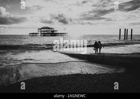 BRIGHTON, Großbritannien - 03.November 2019: Reste von Brighton Pier. Die Silhouetten, die laufen am Strand, Wellen erzeugen Wellen am Ufer, Ocean Spa Stockfoto