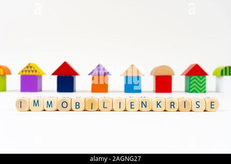 Holzblock mit Buchstaben: "immobilienkrise" (Deutsch für die Immobilienkrise) vor bunten Spielzeug Häuser Stockfoto