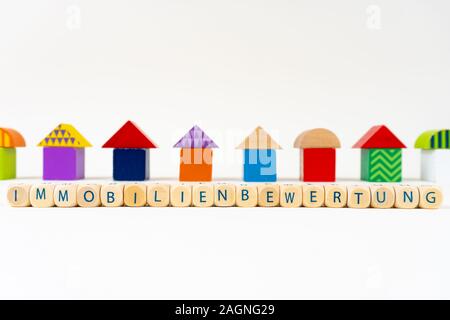 Holzblock mit Buchstaben sagen "Immobilienbewertung" (Deutsch für Immobilien Bewertung) vor bunten Spielzeug Häuser Stockfoto