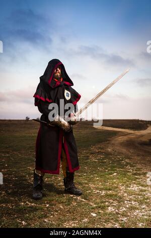 Ritter mit einem Schwert in der Haube vor dem Hintergrund des Abendhimmels. Stockfoto