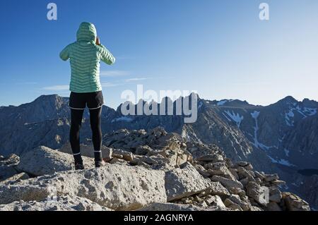 Rückansicht einer Frau in einem puffy Jacke und Strumpfhosen ein Foto von Lone Pine Peak Richtung Mount Langley und Comb Ridge Stockfoto