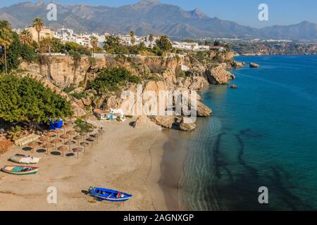 Strandabschnitt in einer Bucht mit Booten an der spanischen Costa del Sol in Nerja. Blick über den Ort, die Berge und die Küste mit blauem Himmel mit blauen ... Stockfoto