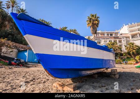 Blau weiß Holz- Boot auf den Strand von der spanischen Mittelmeerküste, Costa del Sol. Sandstrand von Tag im Sonnenlicht mit Palmen und Gebäuden Stockfoto